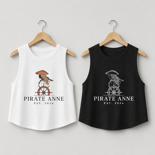 Two sleeveless tank top shirts on wooden hangers against a light gray background. The left shirt is white with a pirate-themed graphic and the text 'PIRATE ANNE EST.