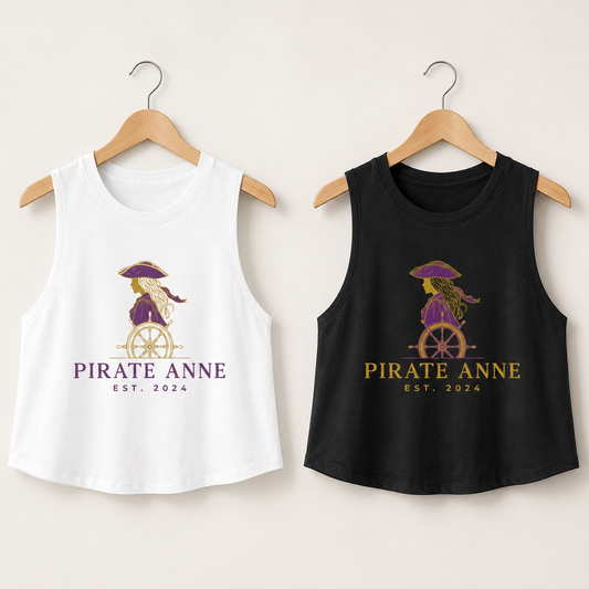 Two sleeveless tank top crop shirts on wooden hangers, one white and one black, both featuring a pirate-themed graphic of a woman on a ship's wheel with the text 'PIRATE ANNE EST. 2024'.